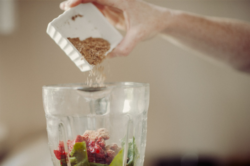 A female adds some ground flaxseed to a blender for a Green Smoothie