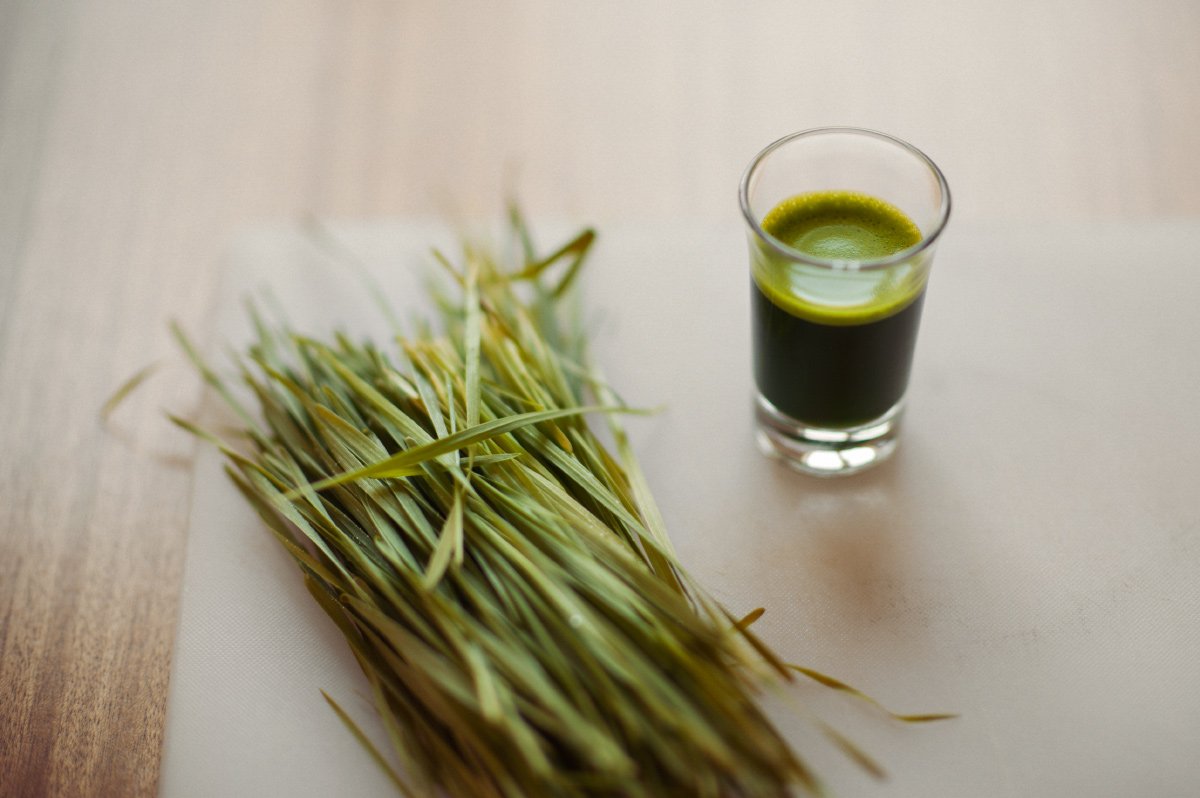 Loose wheat grass sits beside a shot of wheat grass on a chopping board