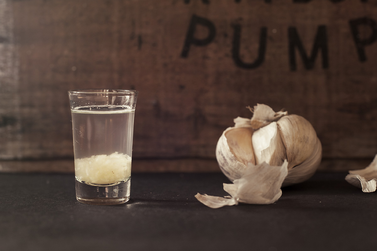 A shot-glass of crushed garlic & water sits alongside a bulb of garlic this is to create good bacteria