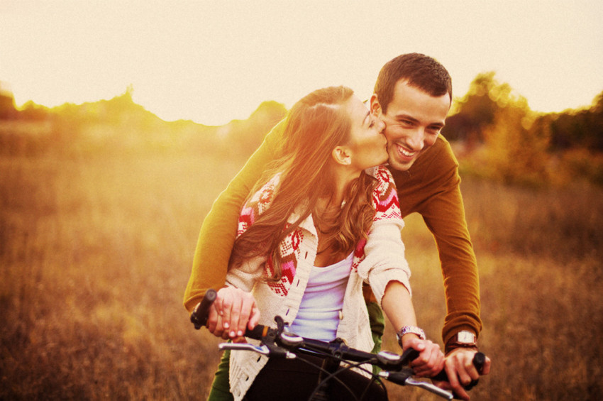 A young man is doubling his girlfriend on a push-bike through a meadow during sunset