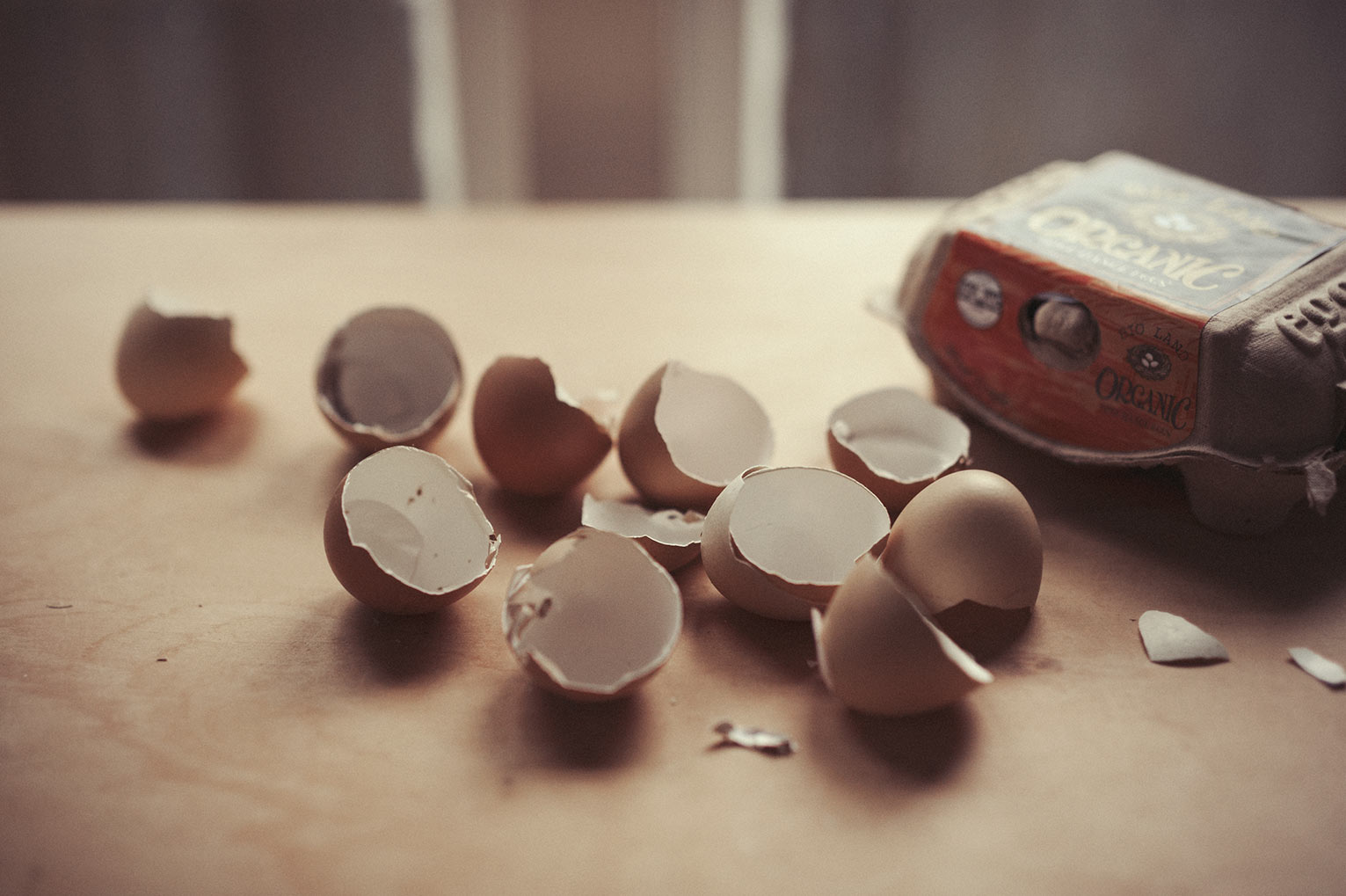 A number of egg shells are displayed next to their carton on a table-top