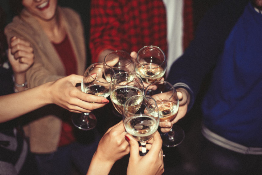 A group of people clink filled wine glasses to indicate drinking alcohol responsibly