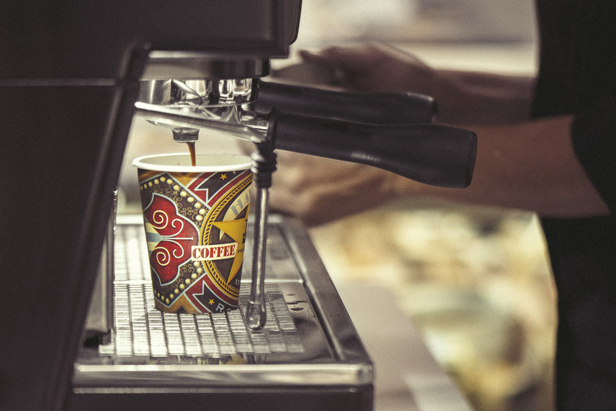An espresso machine drizzles coffee into a colourful paper cup