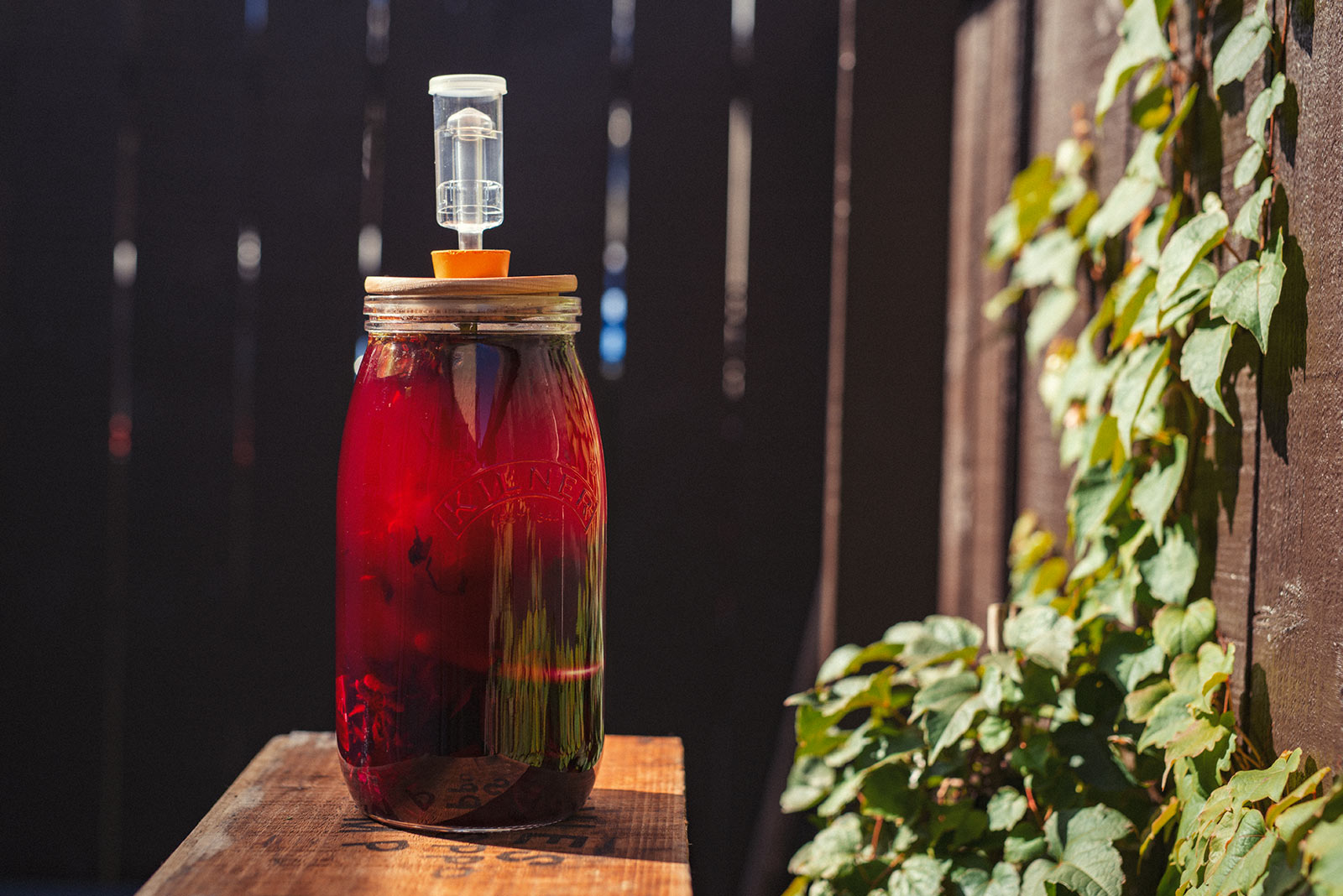 A large jar of fermenting beetroot Kvass sits on a table outside