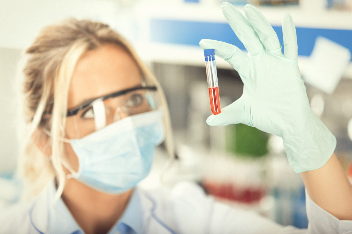 As part of functional testing a female lab technician examines a blood filled test-tube
