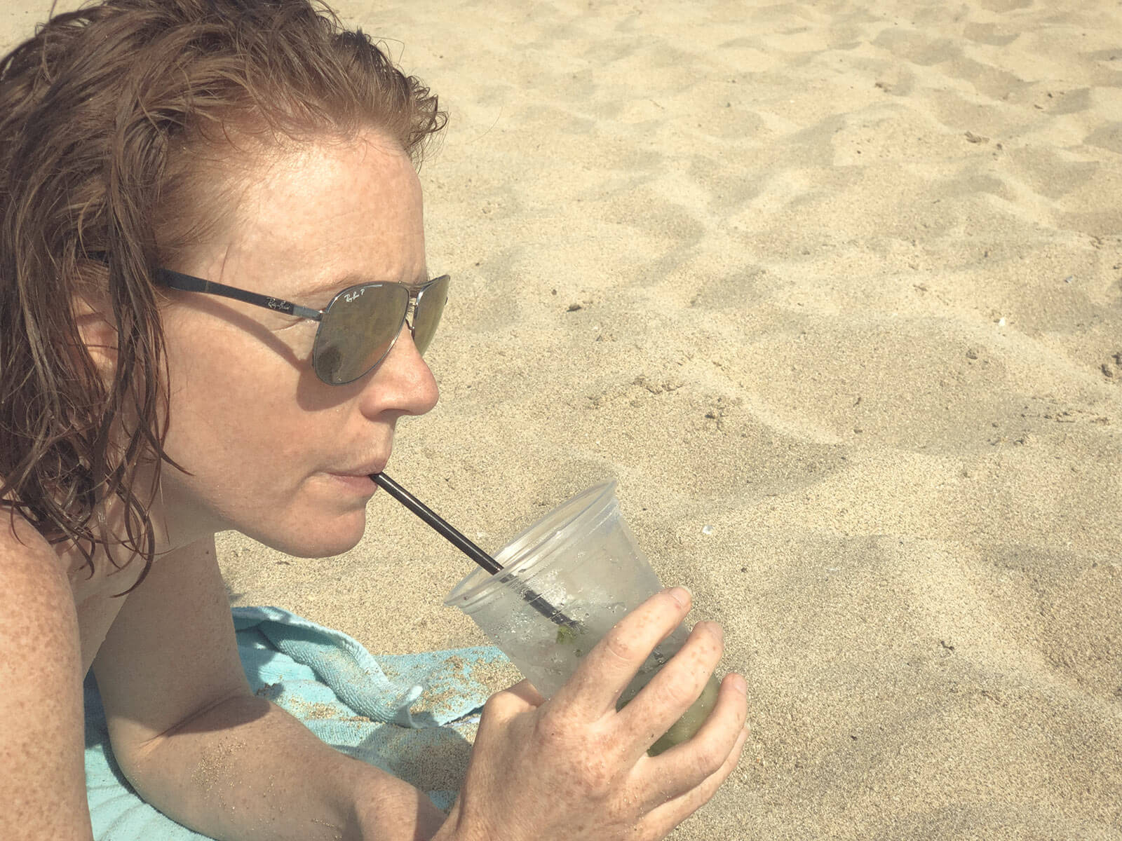 Naturopath, Lisa Fitzgibbon, laying on a beach in Mallorca sipping a Mojito