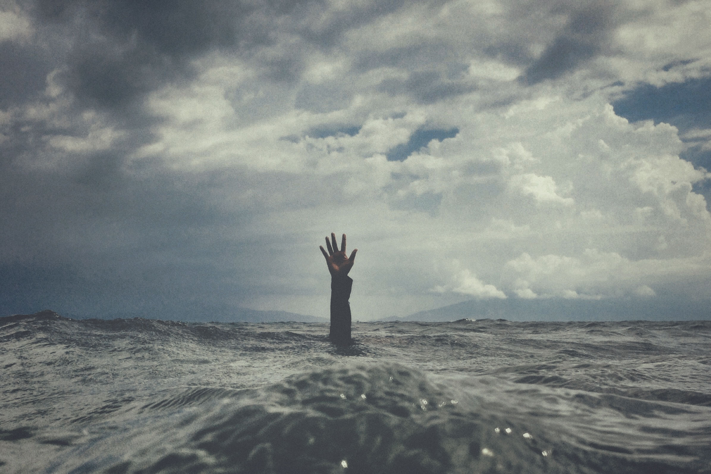 A hand with open palm desperately reaches high out of the ocean to portray living with anxiety