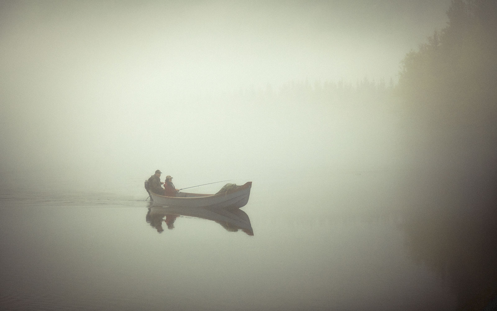 Two fishermen occupy a lone small boat on a misty morning