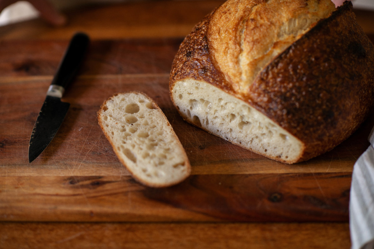 Freshly cut Artisan Sourdough bread and a knife sit on a wooden chopping board